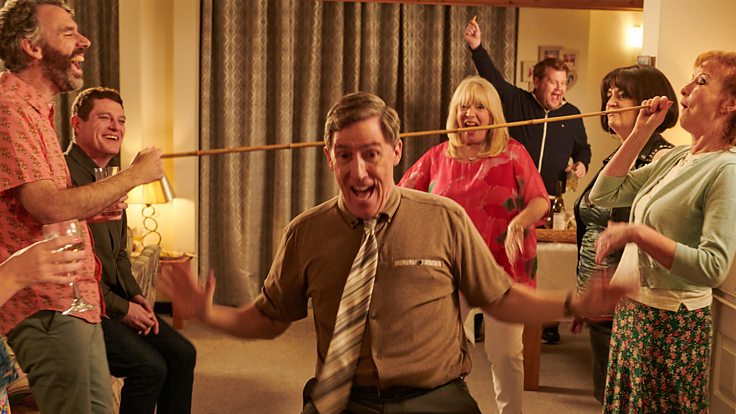 Gavin and Stacey still; family and friends surrounding Uncle Bryn (Rob Brydon) doing a limbo