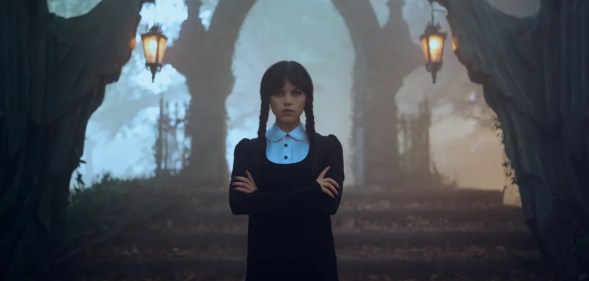 Wednesday Addams shown standing in front of a cemetery