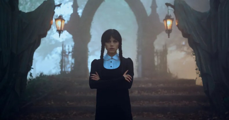 Wednesday Addams shown standing in front of a cemetery