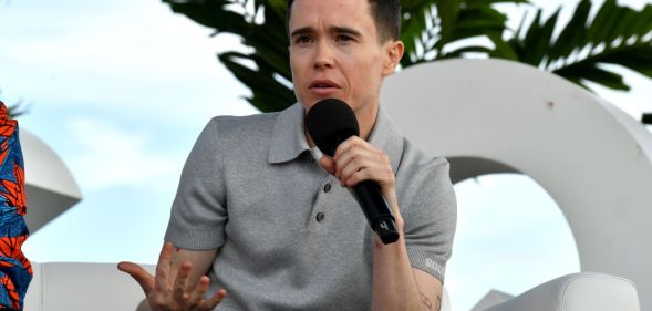 Actor Elliot Page speaking outdoors at a panel event wearing a grey polo shirt