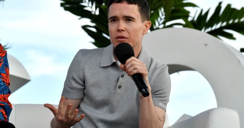 Actor Elliot Page speaking outdoors at a panel event wearing a grey polo shirt