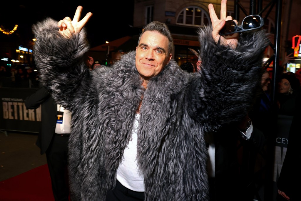 Robbie Williams in a big fluffy fur coat throwing up peace signs