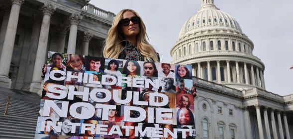 Paris Hilton holding a sign saying "children should not die in treatment"