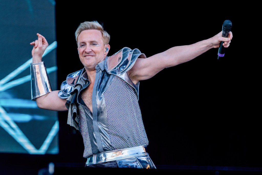 H from Steps band performs on the main stage at Car Fest South. He's wearing a silver outfit with metalic looking armbands and shoulder pads.