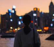 Rear view of young Asian female tourist overlooking the beautiful iconic city skyline of Hong Kong at Victoria harbour at dusk.