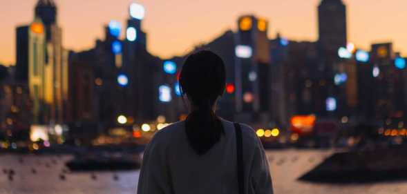 Rear view of young Asian female tourist overlooking the beautiful iconic city skyline of Hong Kong at Victoria harbour at dusk.