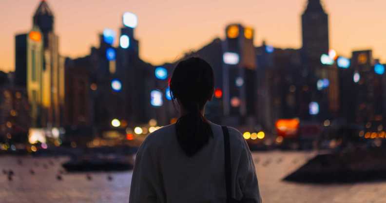 Rear view of young Asian female tourist overlooking the beautiful iconic city skyline of Hong Kong at Victoria harbour at dusk.