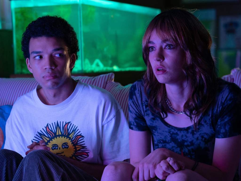 I Saw The TV Glow still: Justice Smith and Brigette Lundy-Paine watching the tv screen that casts a purple glow on them