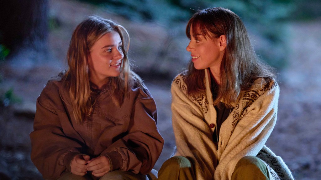 My Old Ass still: Maisy Stella and Aubrey Plaza smiling at eachother sat in front of a campfire