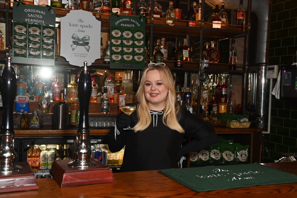 Nicola Coughlan attends the kate spade Arms, she is standing in a black dress behind the bar with a glass of white wine