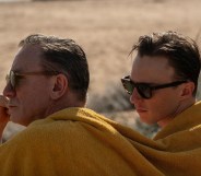 Queer still; Daniel Craig and Drew Starkey sitting together under the same yellow blanket