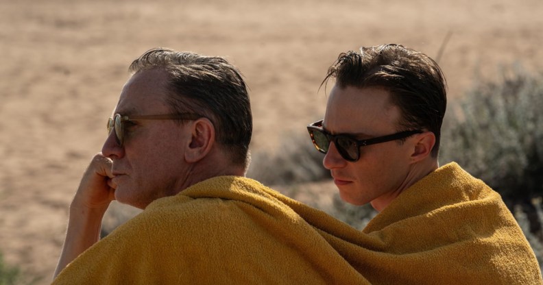 Queer still; Daniel Craig and Drew Starkey sitting together under the same yellow blanket