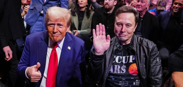 Donald Trump and Elon Musk posing for the camera. Trump in a navy suit and red tie, Musk in a leather jacket and space themed black t shirt.