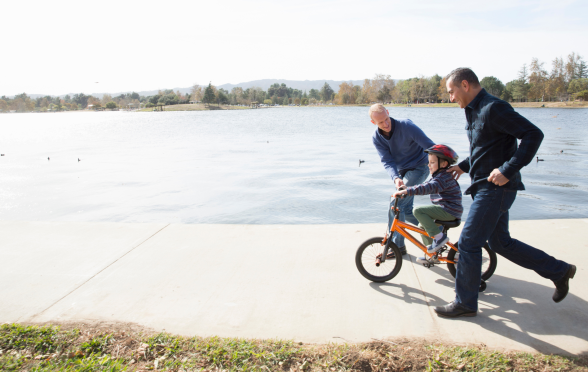 A gay couple teaching their child to ride a bike.