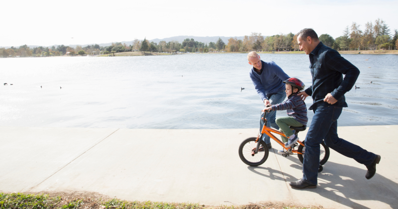 A gay couple teaching their child to ride a bike.