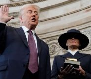 Donald Trump holding his right hand up and his left hand by his side as Melania Trump stands beside him holding two Bibles