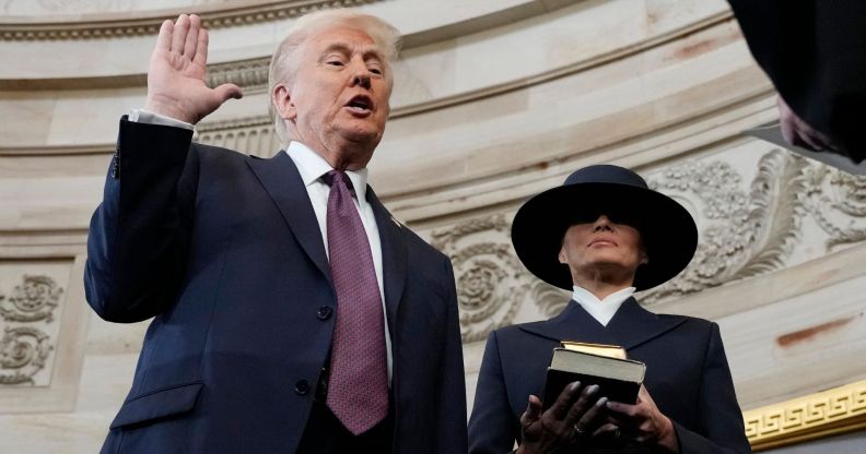 Donald Trump holding his right hand up and his left hand by his side as Melania Trump stands beside him holding two Bibles