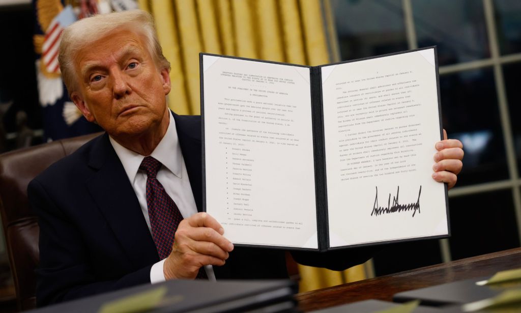 Donald Trump holding up a folder containing an executive order.