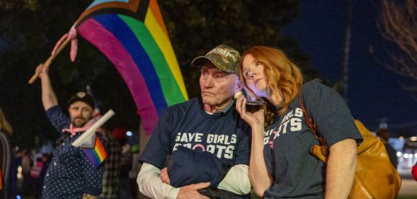 Transgender athlete supporter Kyle Harp, left, of Riverside holds the progress pride flag next to "Save Girls Sports" supporters Lori Lopez and her dad Pete Pickering on December 19, 2024 (Getty)