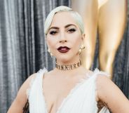 Lady Gaga in a white dress stood against a pair of silver curtains posing.