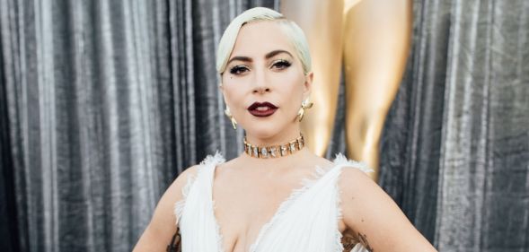 Lady Gaga in a white dress stood against a pair of silver curtains posing.