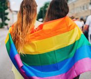 Two people huddled into an LGBT Pride flag.