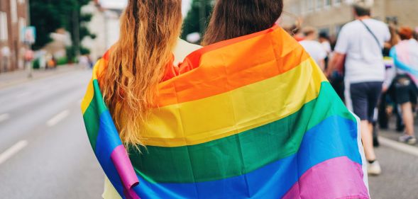 Two people huddled into an LGBT Pride flag.