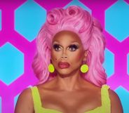 RuPaul in a sleeveless yellow dress and pink wig puckering her lips while sat on the Drag Race All Stars judging panel.