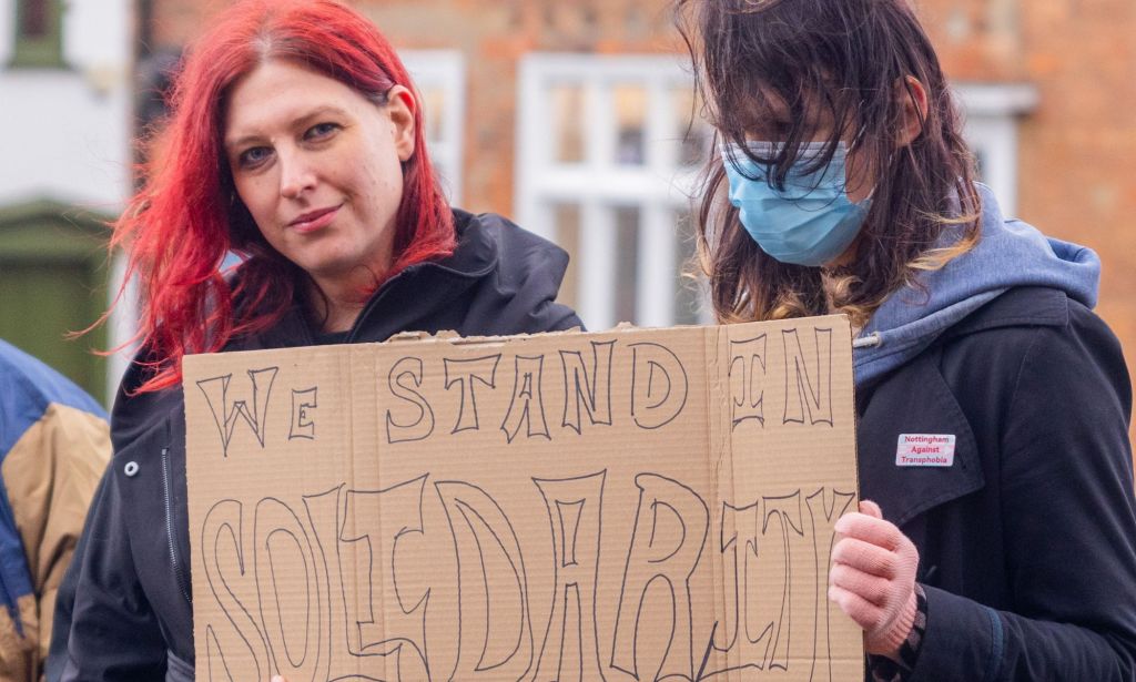 Two protestors holding a sign that reads 'We stand in solidarity'