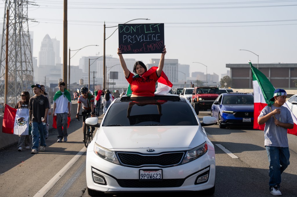 Person holding a protest sign out of a car sunroof