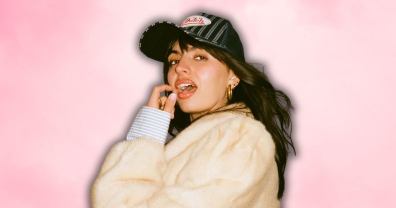 Rebecca Black in a white faux fur jacket and baseball cap, posing with her mouth open and finger and thumb near her face.