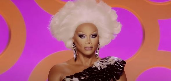 A still of RuPaul smiling watching a lip-sync in episode six of Drag Race season 17