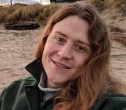 Non-binary American Ryan Castellucci wears a jacket and shirt as they chill on a sandy beach like setting