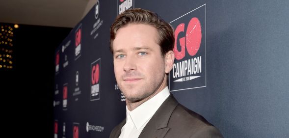 Armie Hammer on a red carpet in 2019 looking at the camera side ways on.