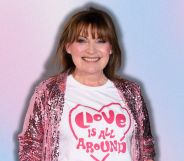 Lorraine Kelly smiling wearing a pink glittery coat and a 'love is all around' t-shirt, she is imposed against a pink and blue background.