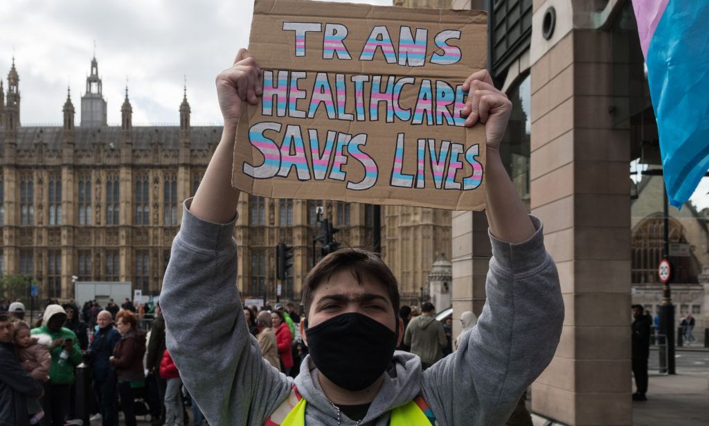 A person holds a sign reading "trans healthcare saves lives."