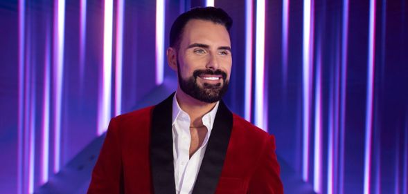 Rylan smiles in a red suit in a promotional image for Doctor Who.