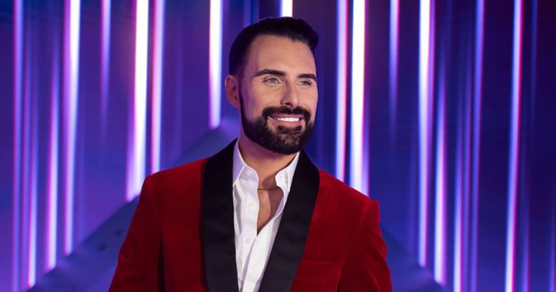 Rylan smiles in a red suit in a promotional image for Doctor Who.