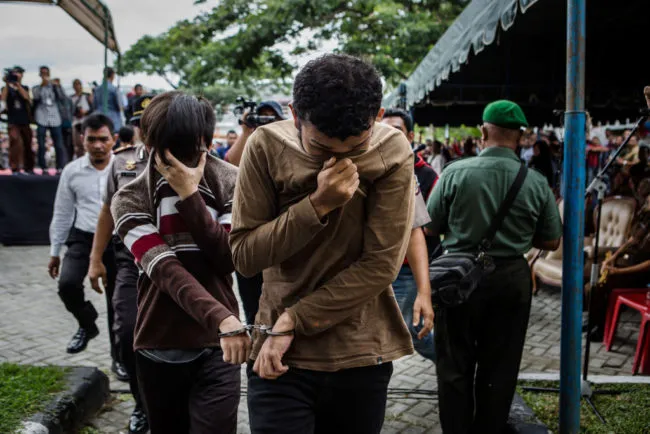 BANDA ACEH, INDONESIA - MAY 23: Indonesian gay couple walk as arrive for caning in public from an executor known as 'algojo' for having gay sex, which is against Sharia law at Syuhada mosque on May 23, 2017 in Banda Aceh, Indonesia. The two young gay men, aged 20 and 23, were caned 85 times each in the Indonesian province of Aceh during a public ceremony after being caught having sex last week. It was the first time gay men have been caned under Sharia law as gay sex is not illegal in most of Indonesia except for Aceh, which is the only province which exercises Islamic law. The punishment came a day after the police arrested 141 men at a sauna in the capital Jakarta on Monday due to suspicion of having a gay sex party, the latest crackdown on homosexuality in the country. (Photo by Ulet Ifansasti/Getty Images)
