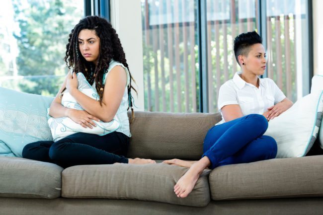 Unhappy lesbian couple sitting on sofa in living room