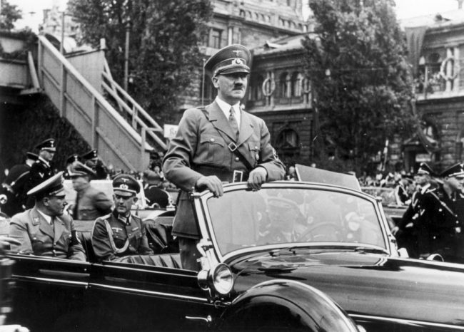 6th September 1938:  The Chancellor of Germany, Adolf Hitler (1889 -1945) standing in his car as he travels through the ancient town of Nuremberg to open the Nazi Congress. In the rear seat of the car on the left is Hitler's secretary and friend Martin Bormann (1900 - 1945).  (Photo by Keystone/Getty Images)