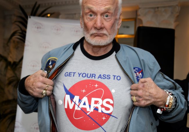 Former NASA astronaut Buzz Aldrin shows the t-shirt he wears promoting Mars exploration on November 12, 2015 in Geneva. Aldrin attended a press conference alongside Soviet cosmonaut Alexei Leonov and Swiss astronaut Claude Nicollier on the eve of a conference in Lausanne entitled "The Moon Race".   AFP PHOTO / FABRICE COFFRINI        (Photo credit should read FABRICE COFFRINI/AFP/Getty Images)