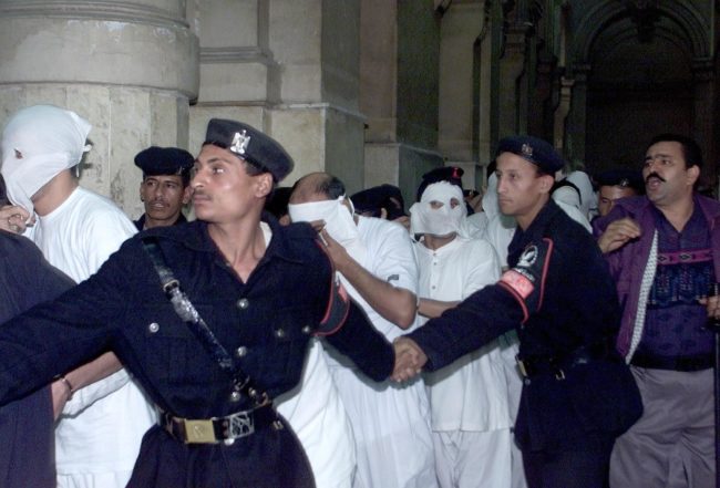 CAIRO, EGYPT:  Egyptians dressed in white with their faces covered, charged with engaging in homosexual activities and scorning Islam, enter a Cairo court under the protection of security men 14 November 2001. One of the 52 men was sentenced to five years in prison and several to three years at the end of their trial. The men were arrested in May following a party on a Nile riverboat. AFP PHOTO/Marwan NAAMANI (Photo credit should read MARWAN NAAMANI/AFP/Getty Images)