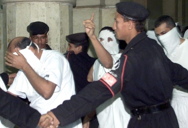 CAIRO, EGYPT: Egyptians with their faces covered, charged with engaging in homosexual activities and scorning Islam, enter a Cairo court under the protection of security men 14 November 2001. One of the 52 men was sentenced to five years in prison and several to three years at the end of their trial. The men were arrested in May following a party on a Nile riverboat. AFP PHOTO/Marwan NAAMANI (Photo credit should read MARWAN NAAMANI/AFP/Getty Images)