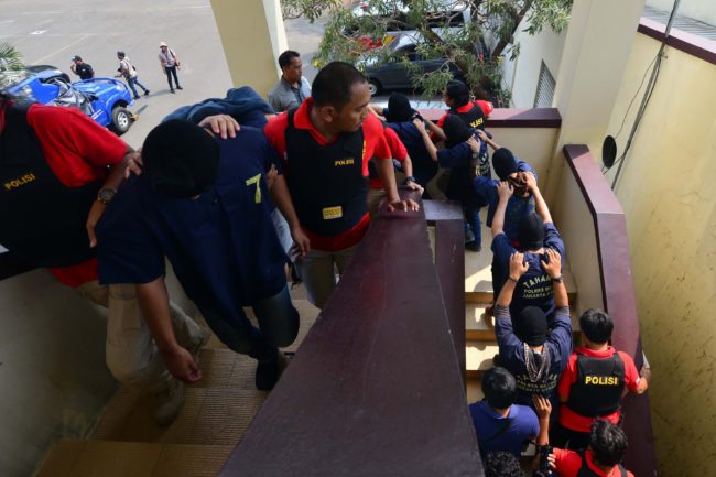 Indonesian police guard men arrested in a recent raid during a press conference at a police station in Jakarta on May 22, 2017.  Indonesian police have detained 141 men who were allegedly holding a gay party at a sauna, an official said on May 22, the latest sign of a backlash against homosexuals in the Muslim-majority country. / AFP PHOTO / FERNANDO        (Photo credit should read FERNANDO/AFP/Getty Images)