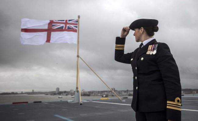 A naval officer looks up at the fluttering White ensign flag hoisted at the stern during the Commissioning Ceremony for the Royal Navy aircraft carrier HMS Queen Elizabeth at HM Naval Base in Portsmouth, southern England on December 7, 2017.  Her Majesty The Queen, accompanied by Her Royal Highness The Princess Royal, attended the Commissioning Ceremony of the aircraft carrier HMS Queen Elizabeth, the largest warship ever built for the Royal Navy.  / AFP PHOTO / POOL / RICHARD POHLE        (Photo credit should read RICHARD POHLE/AFP/Getty Images)