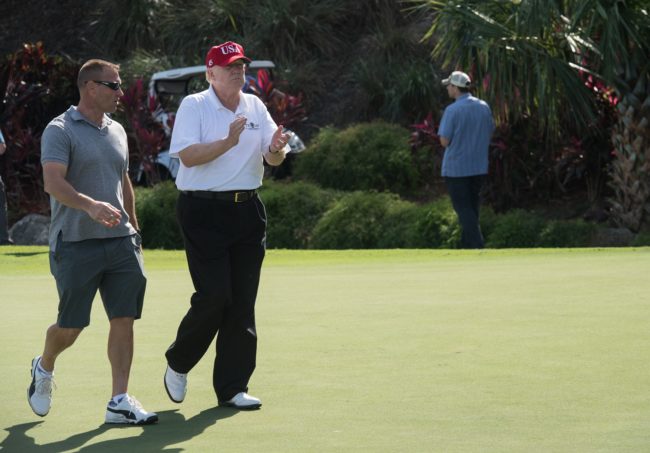 US President Donald Trump walks with US Coast Guard Chief Warrant Officer Gene Gibson, commanding officer of the Lake Worth Inlet Station, during an invitation for Coast Guard service members to play golf at Trump International Golf Course in Mar-a-Lago, Florida on December 29, 2017. The President invited members of the Coast Guard to play golf to thank them personally for their service of patrolling the waters near Palm Beach and Mar-a-Lago. / AFP PHOTO / NICHOLAS KAMM (Photo credit should read NICHOLAS KAMM/AFP/Getty Images)