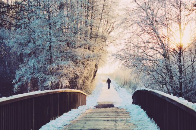 Man walking across snowy bridge into forest