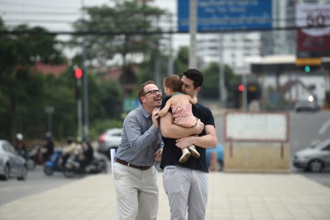 TOPSHOT - American Gordon Lake (L) and his Spanish husband Manuel Valero (R) play with their daughter Carmen after a hearing at The Central Juvenile and Family Court in Bangkok on March 30, 2016. A foreign same-sex couple battling a local Thai surrogate for custody over their infant daughter said on March 30 their lives had been "destroyed" by the 14-month legal war that has prevented their family from returning home. Manuel Valero, from Spain, and his American husband Gordon Lake were blocked from leaving Thailand with their daughter Carmen after the surrogate refused to sign necessary paperwork following the birth last January. / AFP / LILLIAN SUWANRUMPHA (Photo credit should read LILLIAN SUWANRUMPHA/AFP/Getty Images)