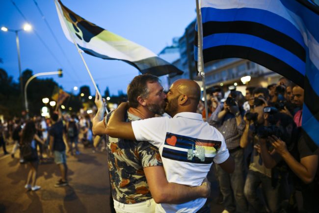 Two men waving flags kiss during the  annual Gay Pride parade  in central Athens on June 13, 2015.  Greece's radical-left government on June 10, 2015, proposed a bill to grant same-sex couples the right to a civil union, two years after the European Court of Human Rights condemned the country's existing legislation as discriminatory. AFP PHOTO / ANGELOS TZORTZINIS        (Photo credit should read ANGELOS TZORTZINIS/AFP/Getty Images)
